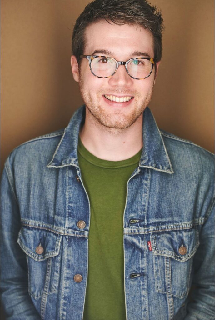 Headshot of Joshua with glasses and jean jacket with a green shirt